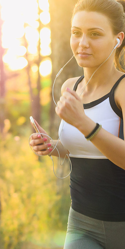 Freizeit und Sport in Ostbayern - junge Frau mit Kopfhörern joggt im Wald bei sonnigem Wetter